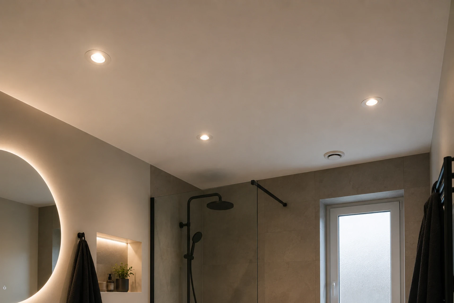 Moderne badeværelse med bruser og væglampe i minimalistisk design.